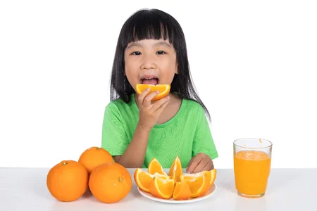 76779003-feliz-niña-china-asiática-comiendo-naranja-en-fondo-blanco-aislado